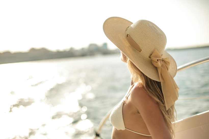 Back view of slim female in bikini top and straw hat enjoying trip on cruise boat on sunny day while relaxing during summer vacation and looking away