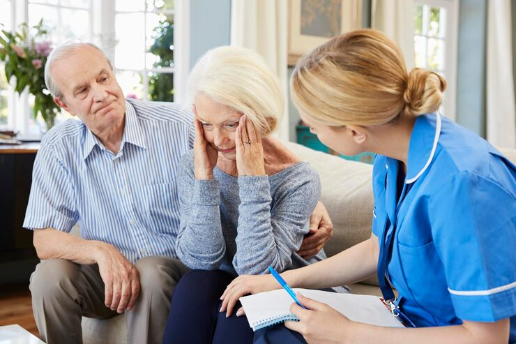 Nurse supporting elderly couple at home while discussing health concerns